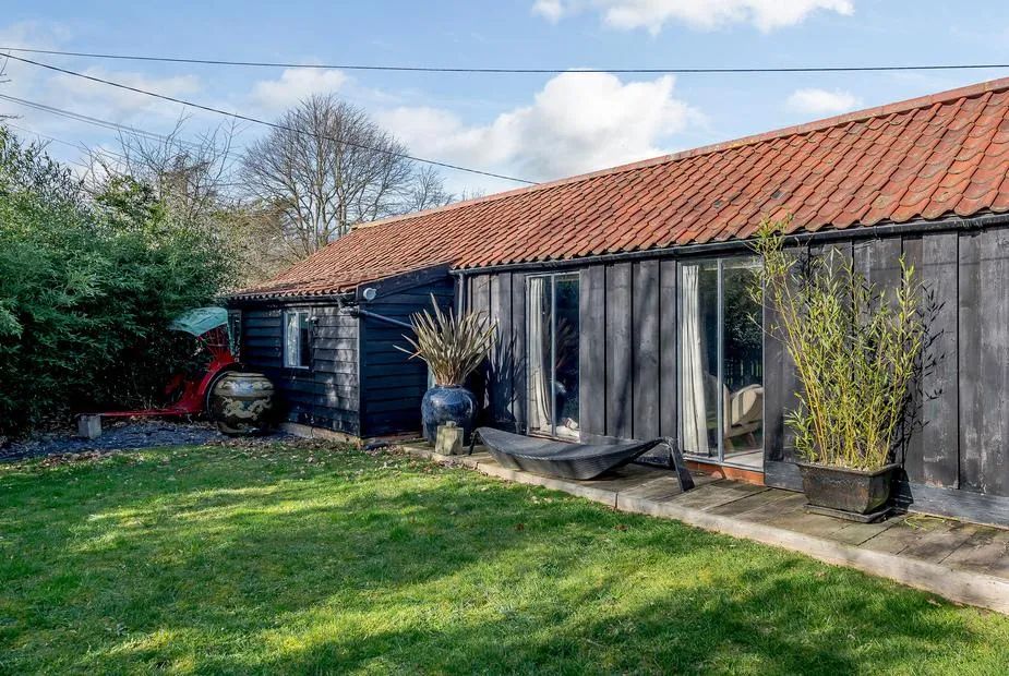 Black timber-clad barn with red-tiled roof, patio doors opening onto a grass lawn