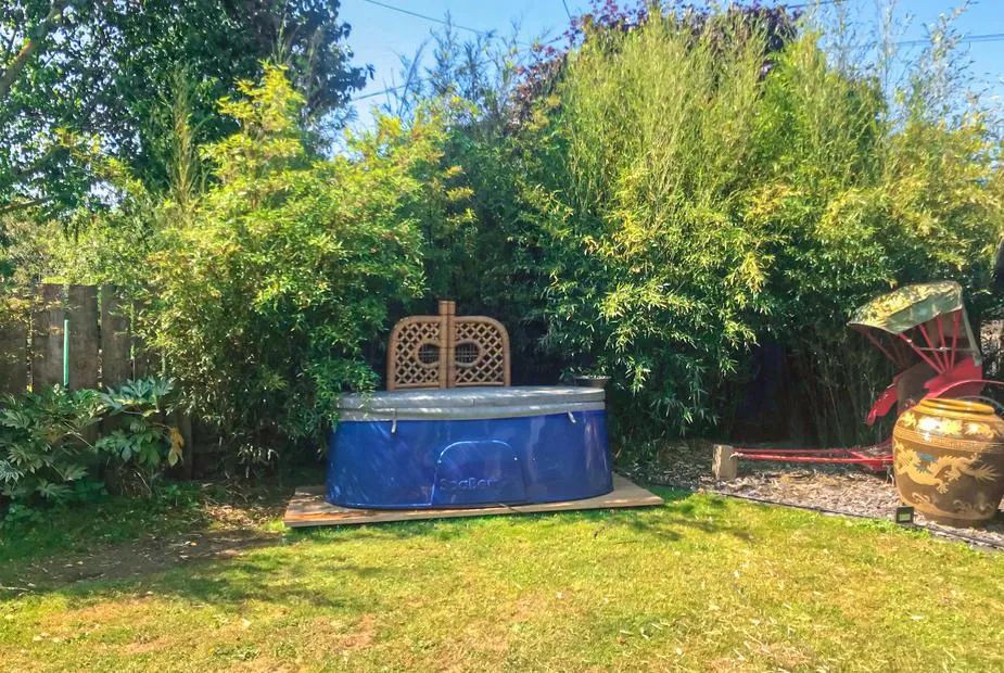 Blue oval hot tub in a garden enclosed by tall reed privacy screens with a bench behind