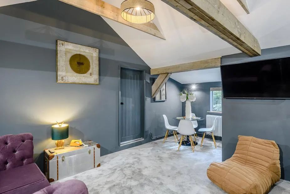 Vaulted living area with dark blue walls, exposed beams, mustard floor chair and small dining table