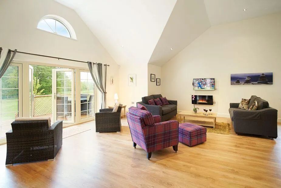 Vaulted living room with tartan armchair, grey sofas, wall-mounted TV and bifold doors to the deck
