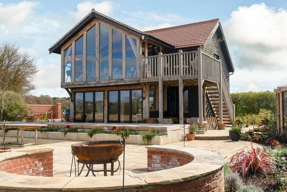 Wood-clad barn with glazed front, balcony, external staircase and a fire pit in a stone enclosure