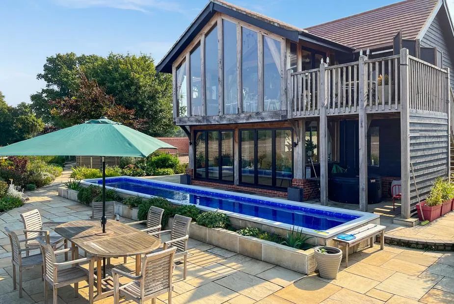 Wood-clad barn with double-height glazed front, upper balcony and a lap pool on the stone terrace
