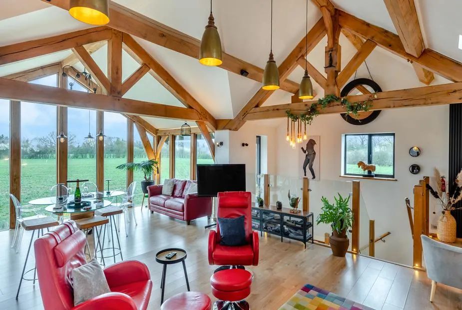 Vaulted living area with exposed oak trusses, red leather armchairs and floor-to-ceiling windows to the countryside