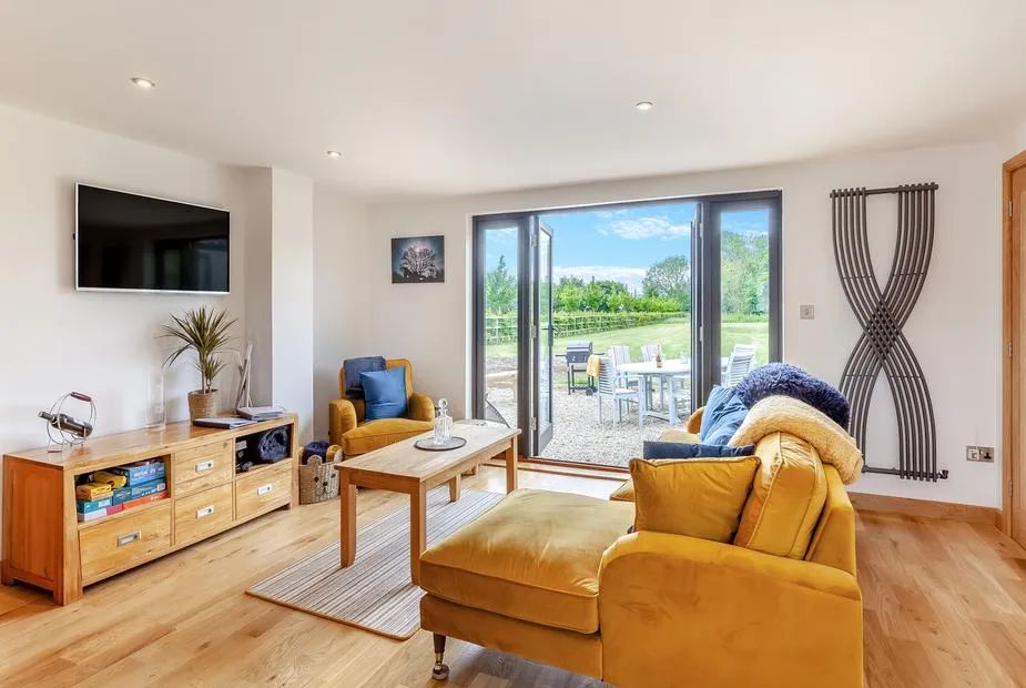 Open-plan living room with mustard armchair, sofa, wall-mounted TV and bifold doors to the garden