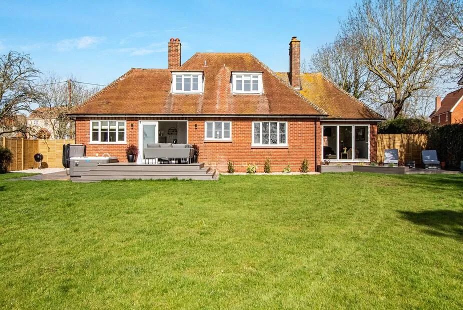 Red brick country house with tile roof, dormers and lawn leading to a decked seating area