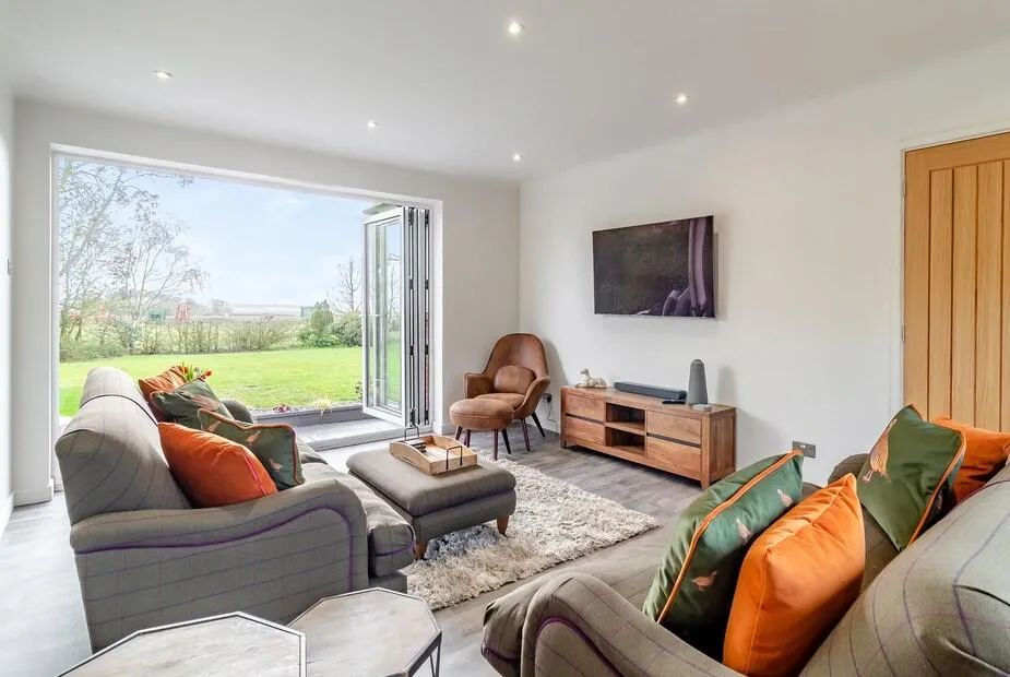 Open-plan living room with grey tweed sofas, orange cushions and bifold doors opening to the garden