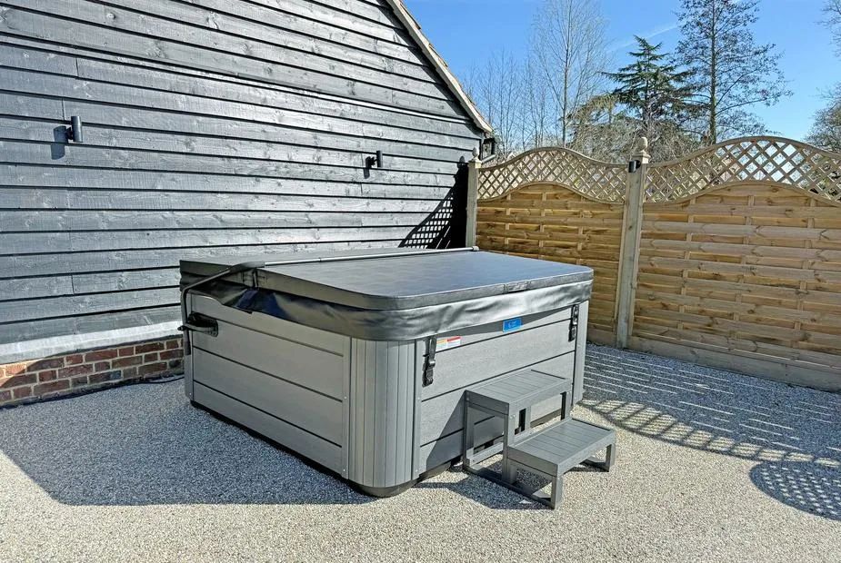 Covered hot tub on gravel beside wood cladding with a slatted privacy screen