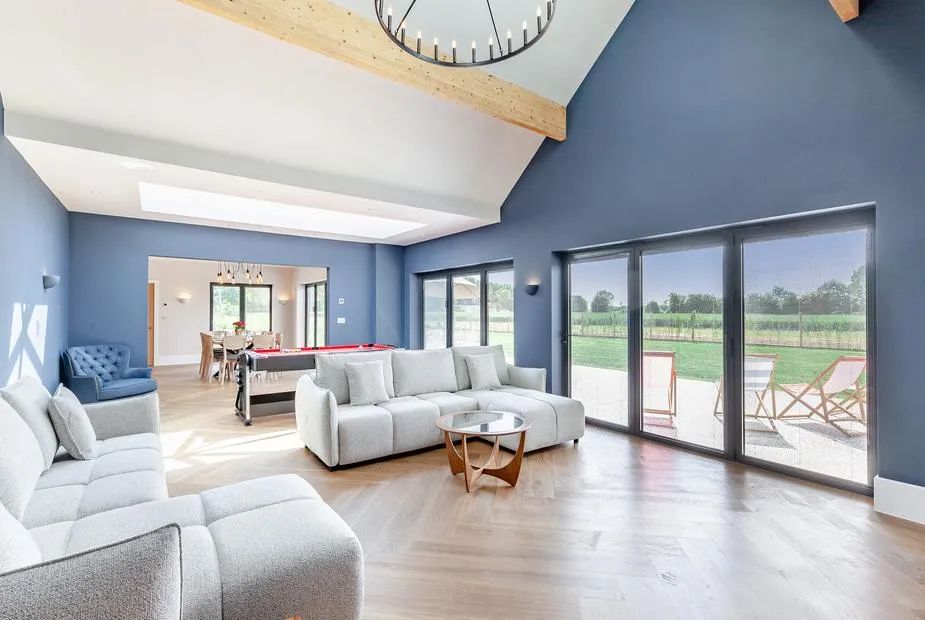 Open-plan living room with deep blue walls, grey sofas, pool table and bifold doors to the garden