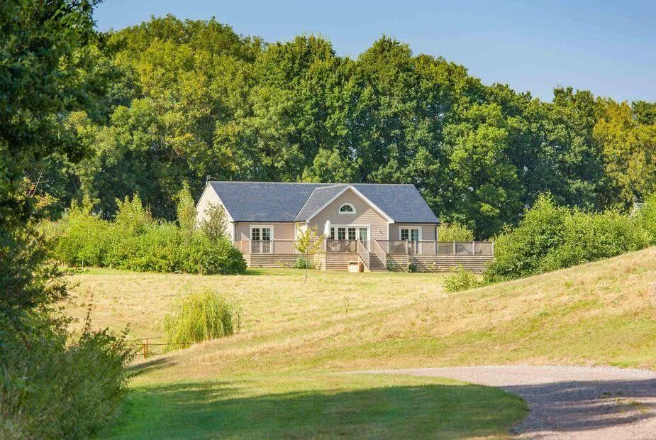 Single-storey lodge on a hillside meadow with pitched slate roof and mature trees behind