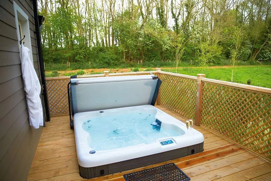 Bubbling hot tub on a timber deck with lattice privacy fencing, towel hanging and meadow views beyond